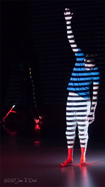 A person stand with arm raised, stripes of light projected onto their body