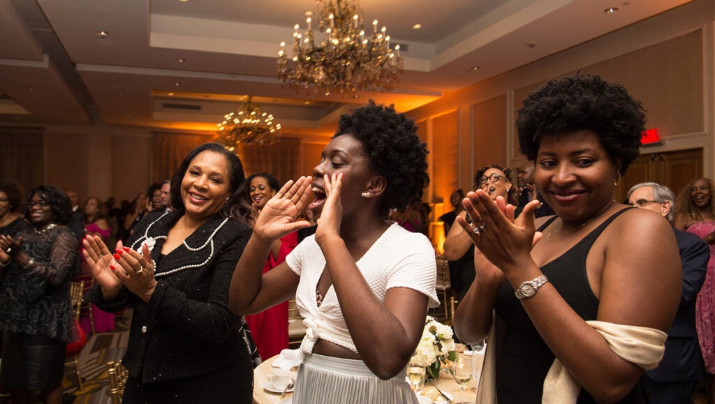 Three women cheer and clap at an event in a ballroom