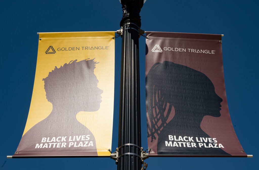 Two banners on a light pole display Black Lives Matter messages