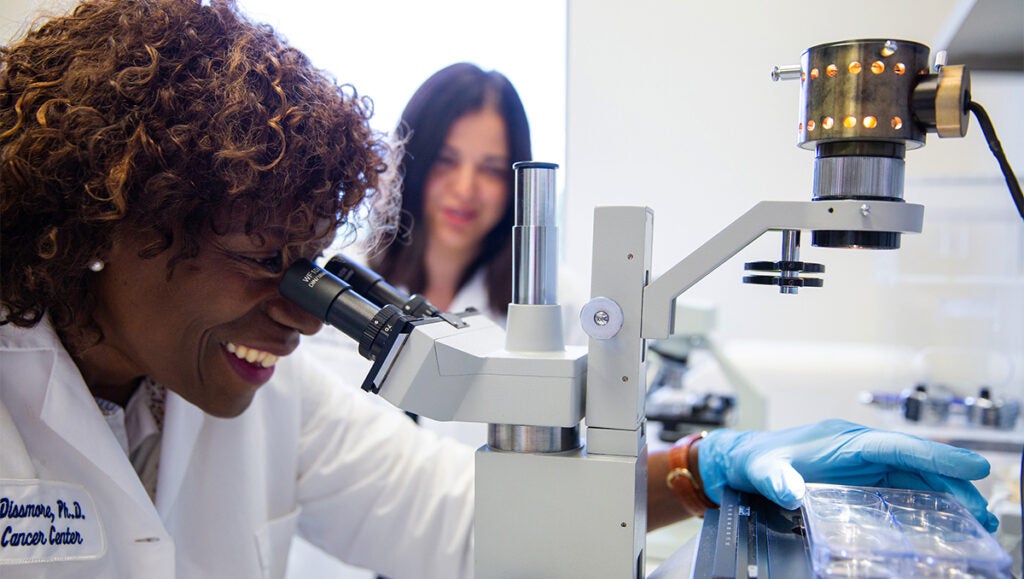 A researcher adjusts a specimen under a microscope while another researcher looks on